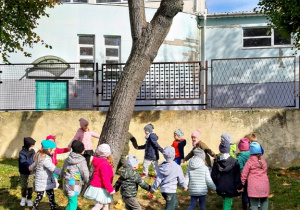 Dzieci śpiewają i tańczą wokół drzewa.